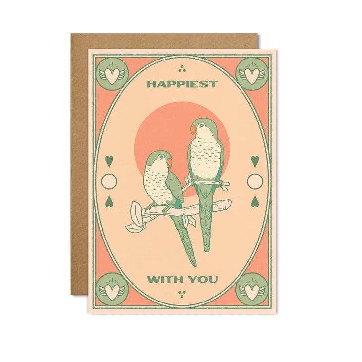 A greetings card with a light green frame around the sides and an image of two sage green and cream lovebirds on a branch. Shades of peach are the other main colours with small cream hearts surrounded by sage green in the corners. The words &#39;happiest with you&#39; feature in sage green around the birds.