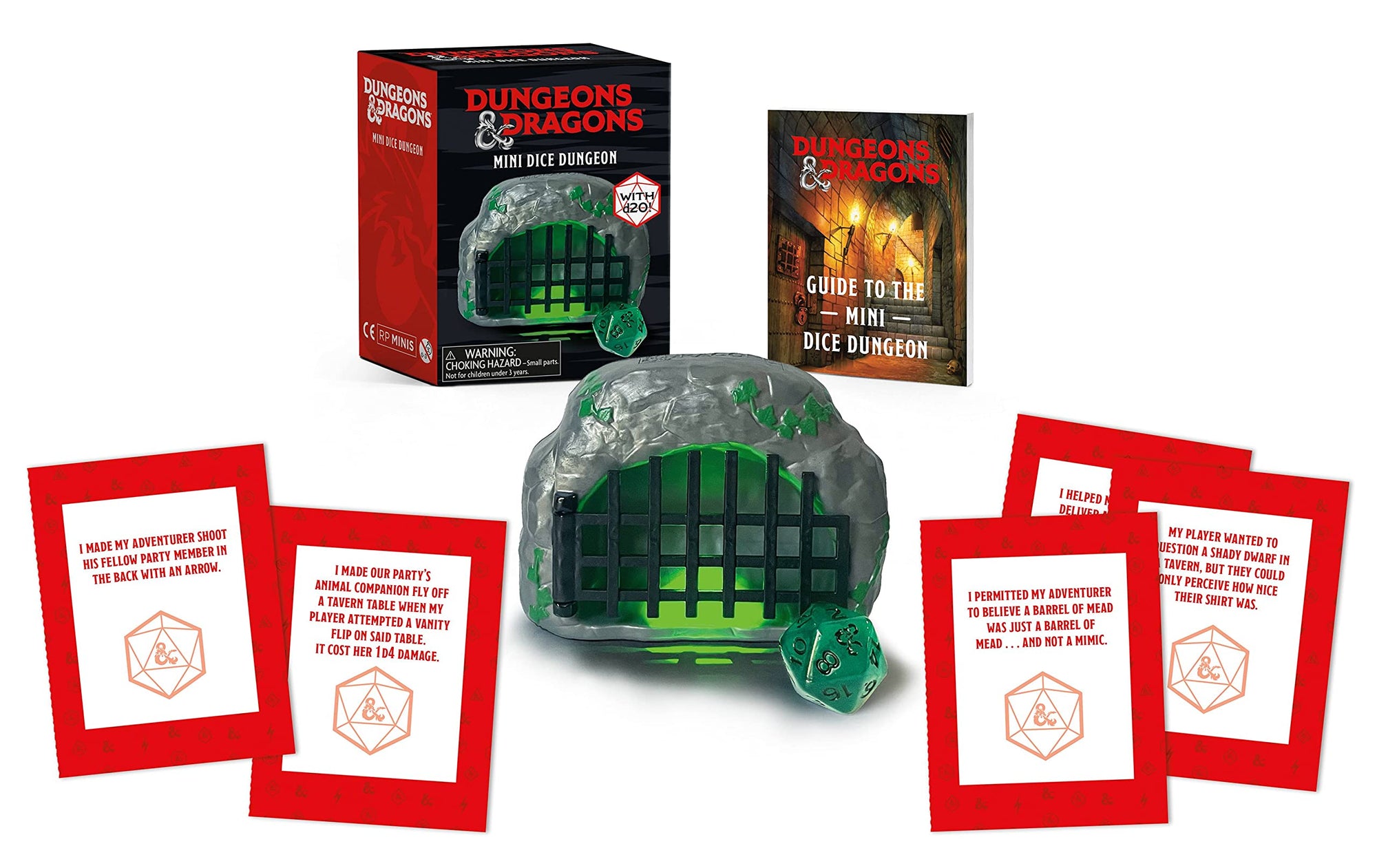 An image of the inside contents of a mini dice dungeon for playing the game Dungeons & Dragons. It includes a glowing cave with a barred gate over it, a D20 dice, some cards and a guide.