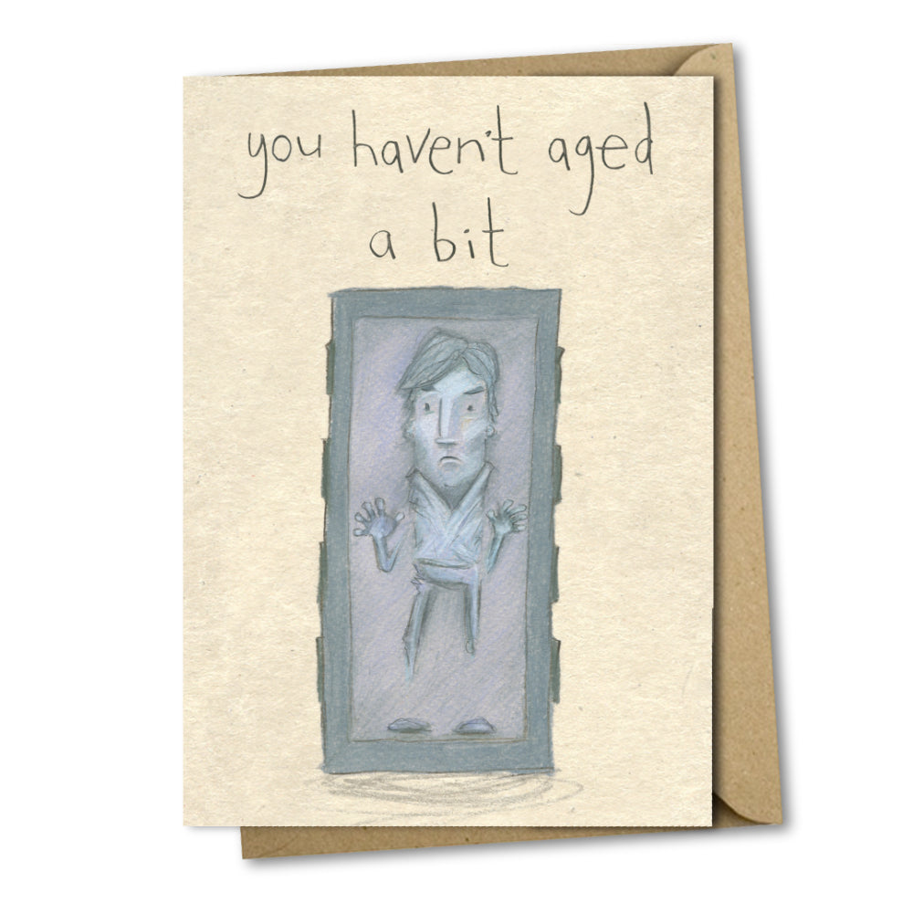 A greetings card with a mottled beige background and above the illustration are the handwritten words 'you haven't aged a bit'. The illustration is of Han Solo from the movie star wars frozen in carbonite.
