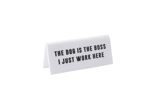 A small white acrylic sign that has in big black capital letters on it &#39;THE DOG IS THE BOSS I JUST WORK HERE&#39;.
