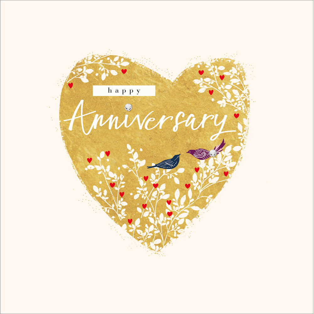 A greetings card with a gold heart, white foliage around the sides and two birds sitting on it. The words written say 'happy anniversary'.