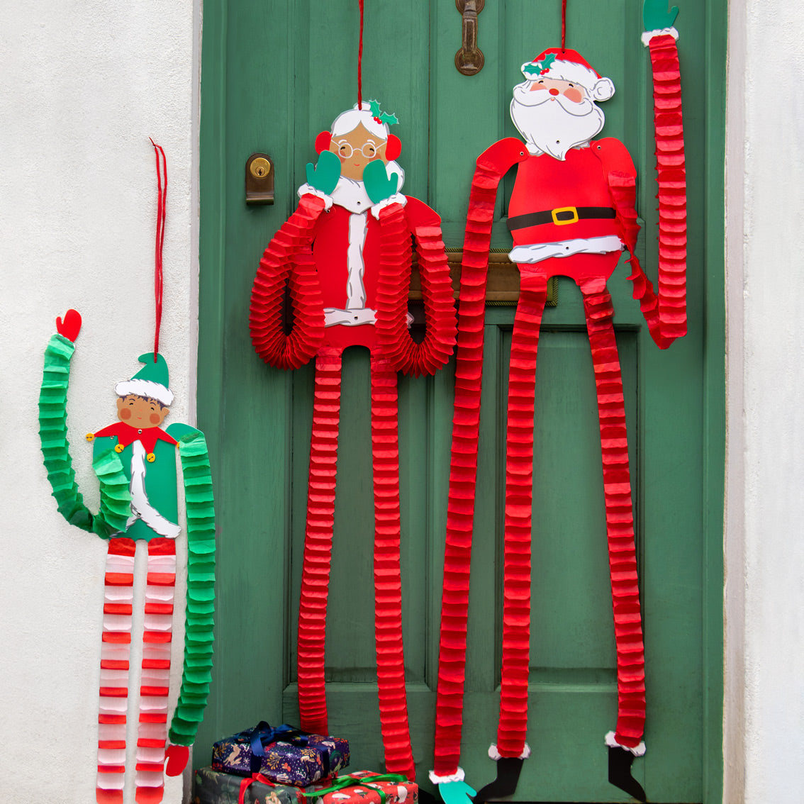 An image of a green house door decorated with Christmas figures with long concertina paper arms and legs.