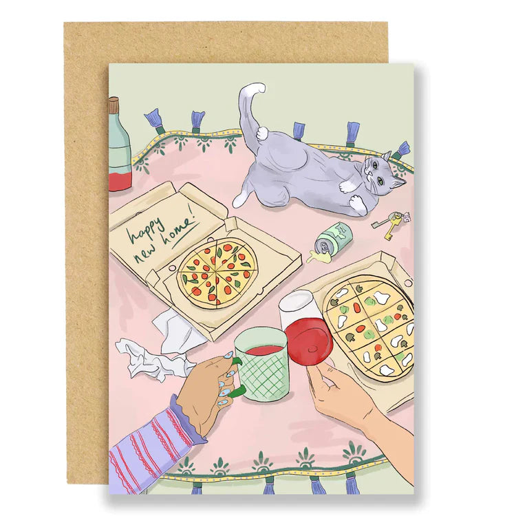 A greetings card with an illustration of a couple eating a takeaway pizza on a circular rug. On the pizza box reads 'happy new home'. The couple are chinking red wine in a glass and mug.