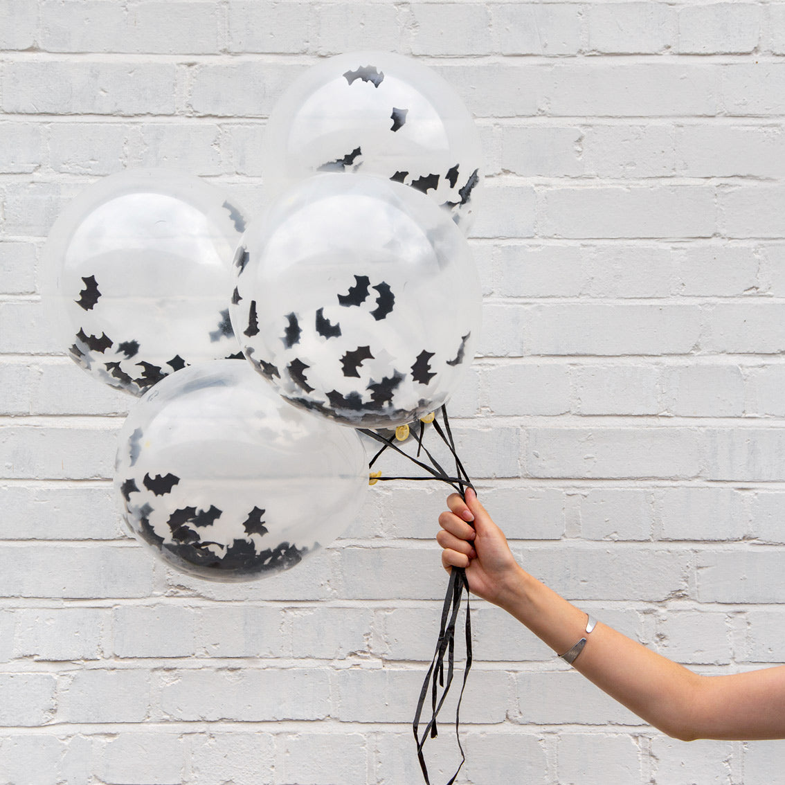 A white person holding a bunch of semi-transparent balloons that feature black bats on the inside.