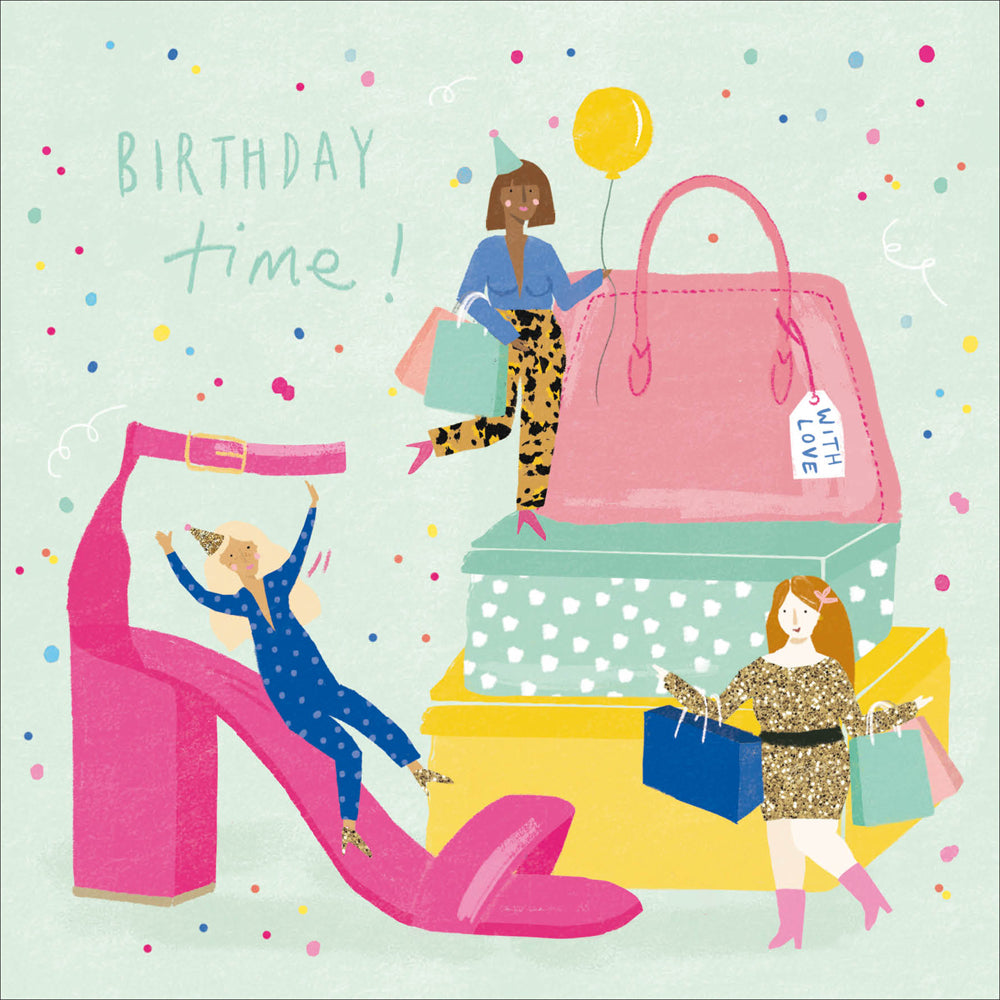 A greetings card with a light green background. It features giant gift boxes, a handbag and a dressy high heeled pink shoe with 3 women of mixed ethnicity. One is sliding down the shoe, one is standing on the boxes holding a balloon and one is carrying shopping bags. The words 'birthday time' feature in green.
