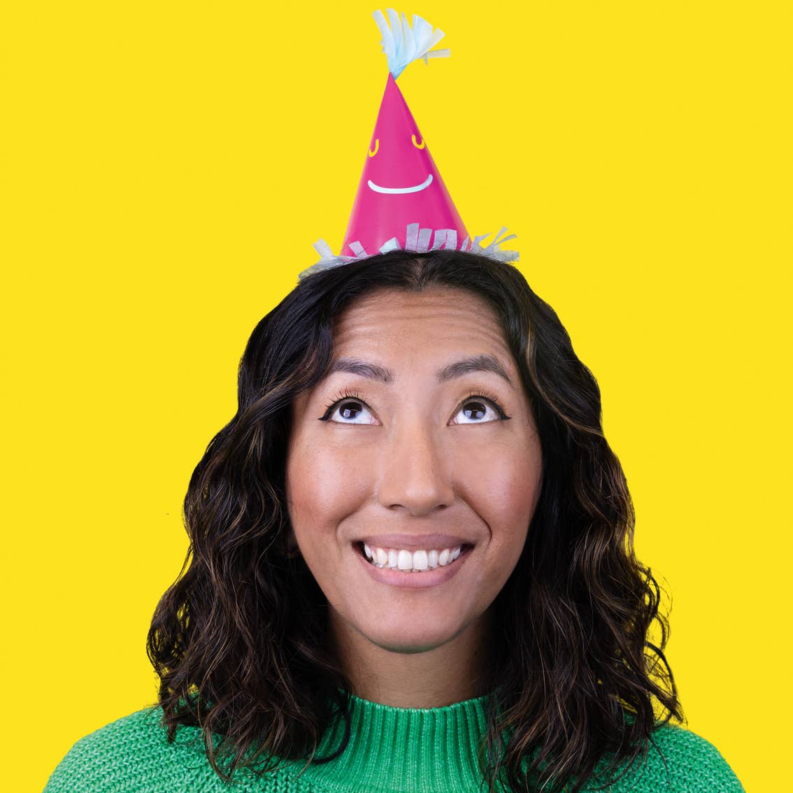 Happy Face Paper Party Hats 5pk - showing a woman with dark brown wavy hair wearing a pink party hat on her head.