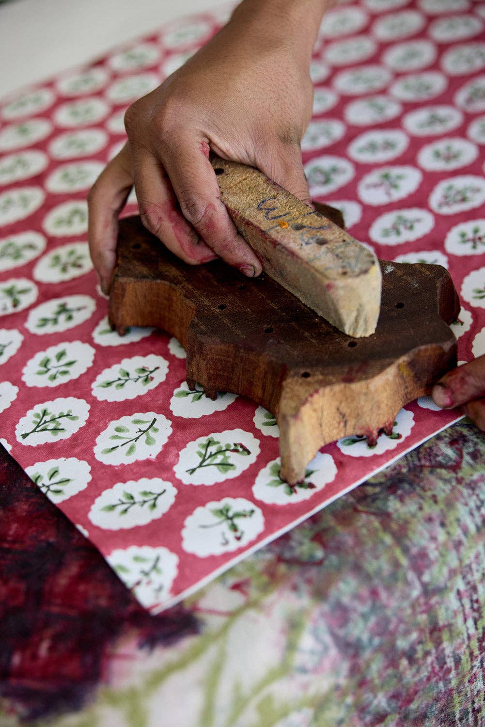 Hand holding a wooden block printing onto a with a floral-patterned wrapping paper sheet.