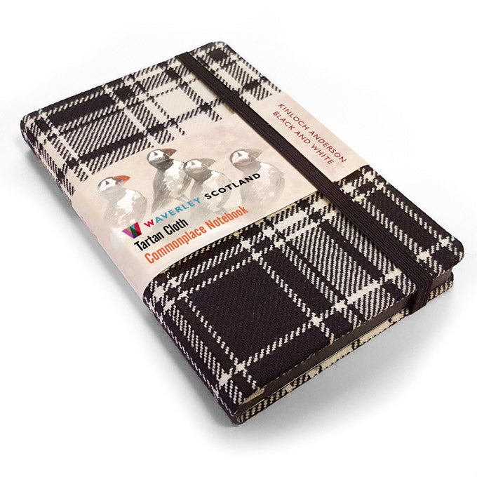 An image of a black and white tartan notebook. It has a black closure band and a paper belly band explaining the product and brand.