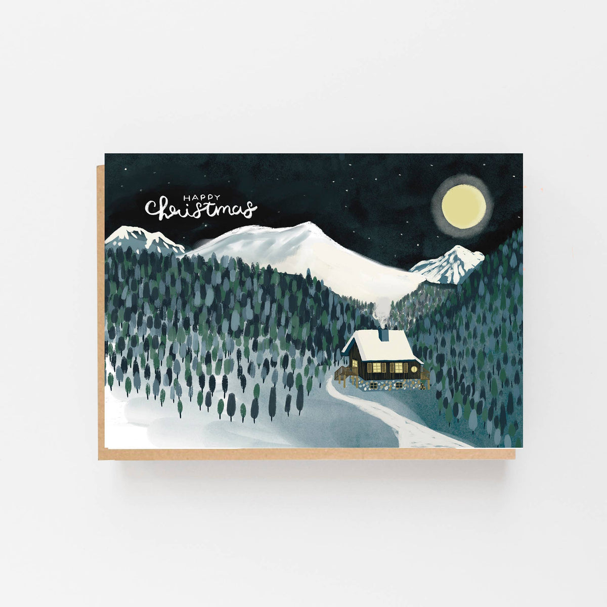 An A6 Christmas greeting card with a kraft paper envelope, featuring an illustration of a snowy mountain landscape at night with a cabin, trees, stars, and a full moon. The card is displayed against a clean white background.