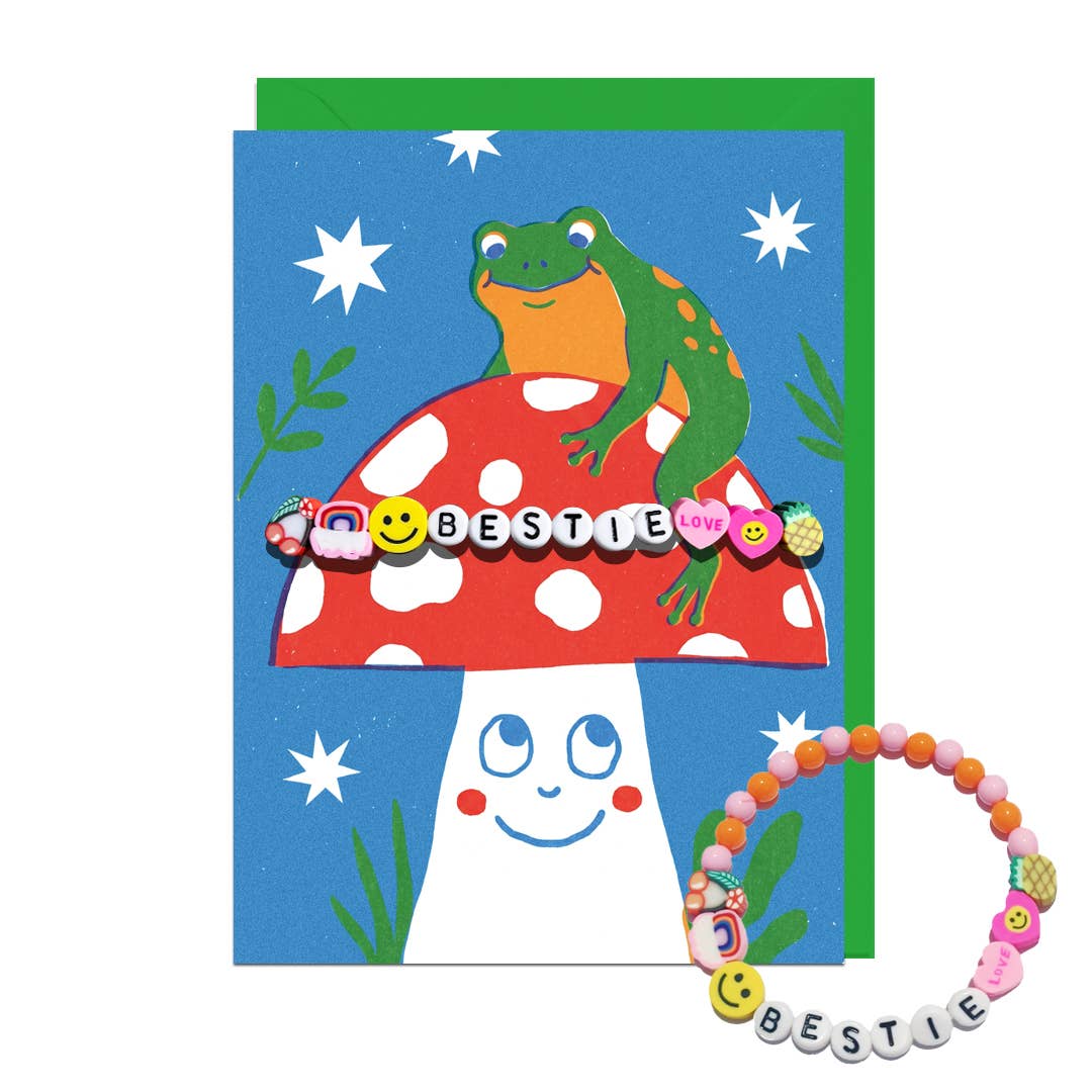 Greetings card with a frog on a mushroom and a bracelet with 'BESTIE' beads on a white background with a green envelope.
