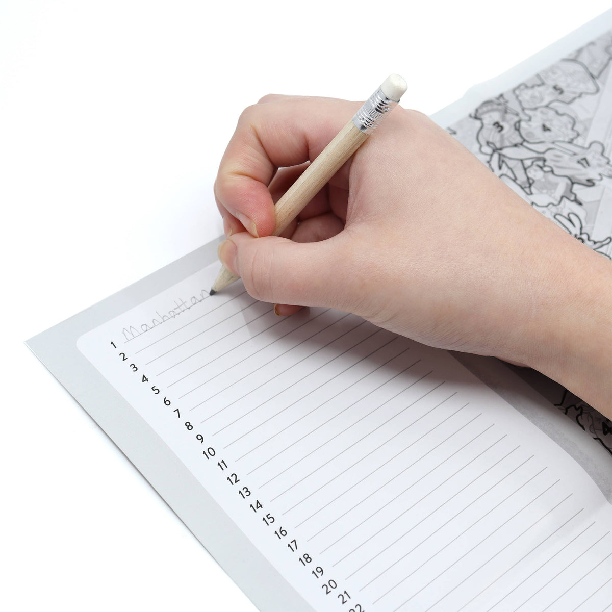 A close-up of a hand holding a wooden pencil and writing on a lined notebook page, with a legend visible in the background on a white surface.