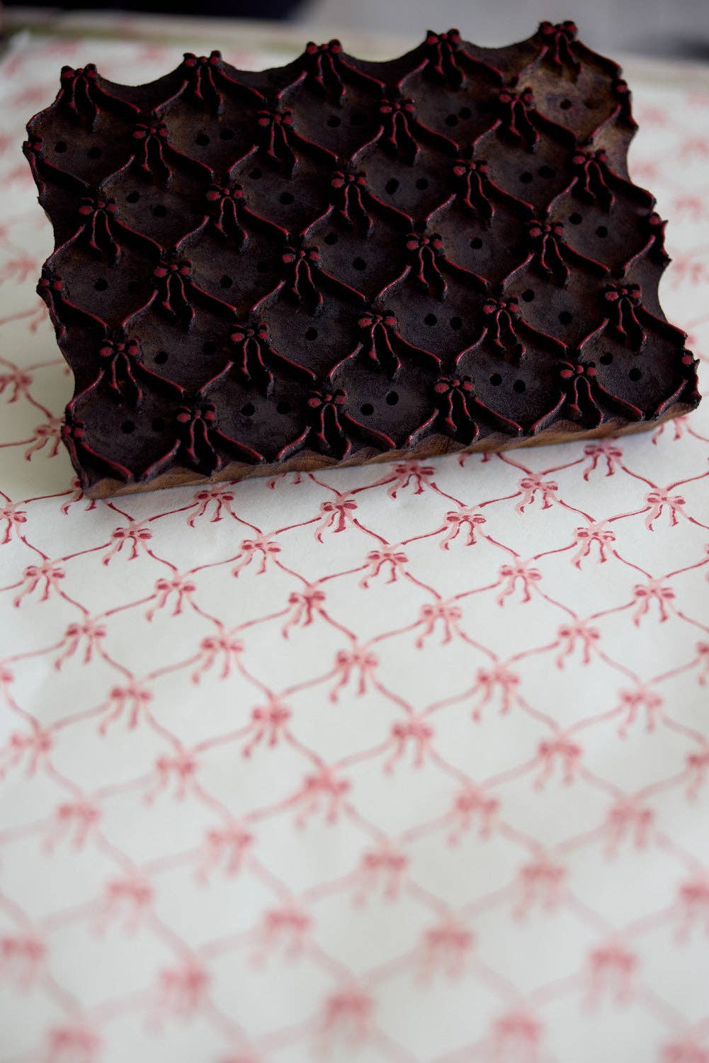 A wooden block resting on a white wrapping paper sheet with pink bows on that has just been printed