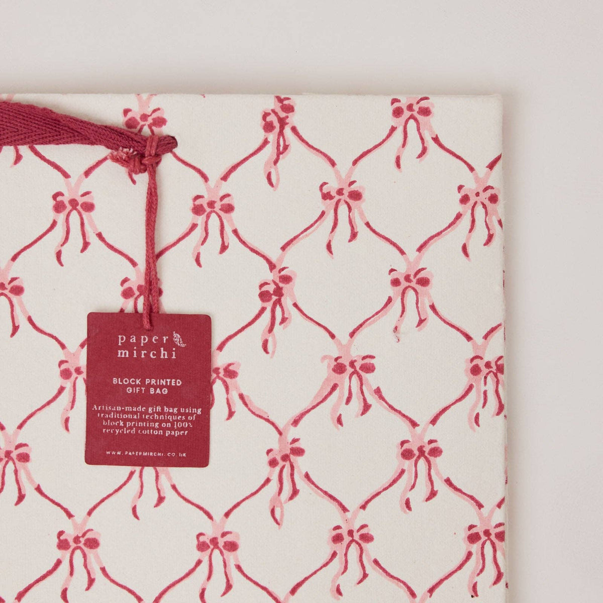 A close up of a large christmas gift bag with pink christmas bow design on a light gray background by paper mirchi at penny black