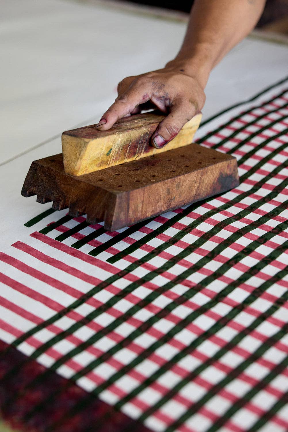 Person using a wooden block printing tool on a checkered wrapping paper