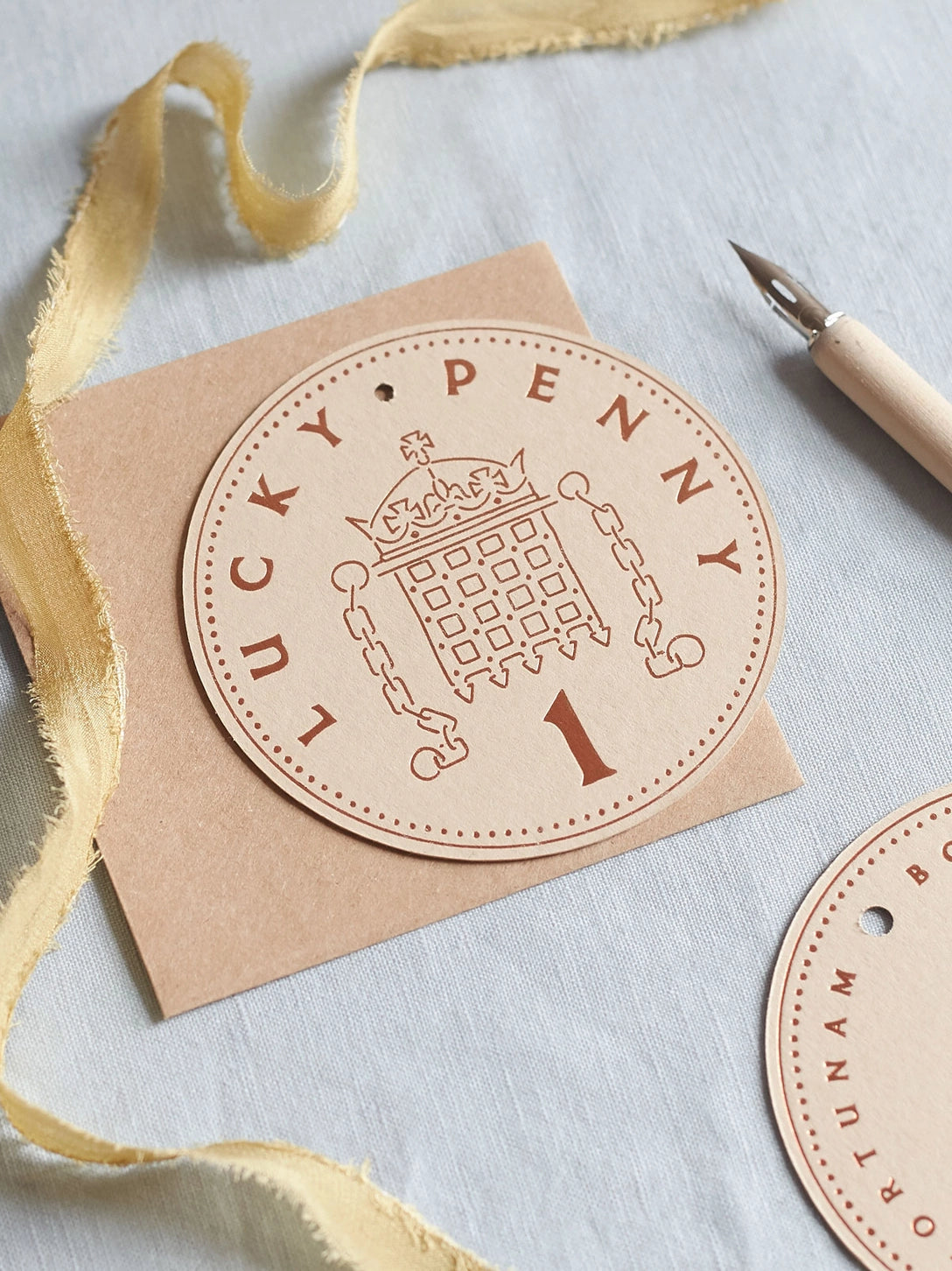 Round beige Lucky Penny notecard with a crown design with a brown envelope - by penny black shown in a table with a pen