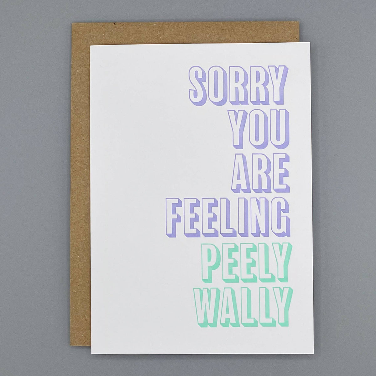 A cream letterpress printed greeting card with the phrase 'SORRY YOU ARE FEELING PEELY WALLY' printed in large outlined letters, shown with a brown kraft envelope on a plain gray background.