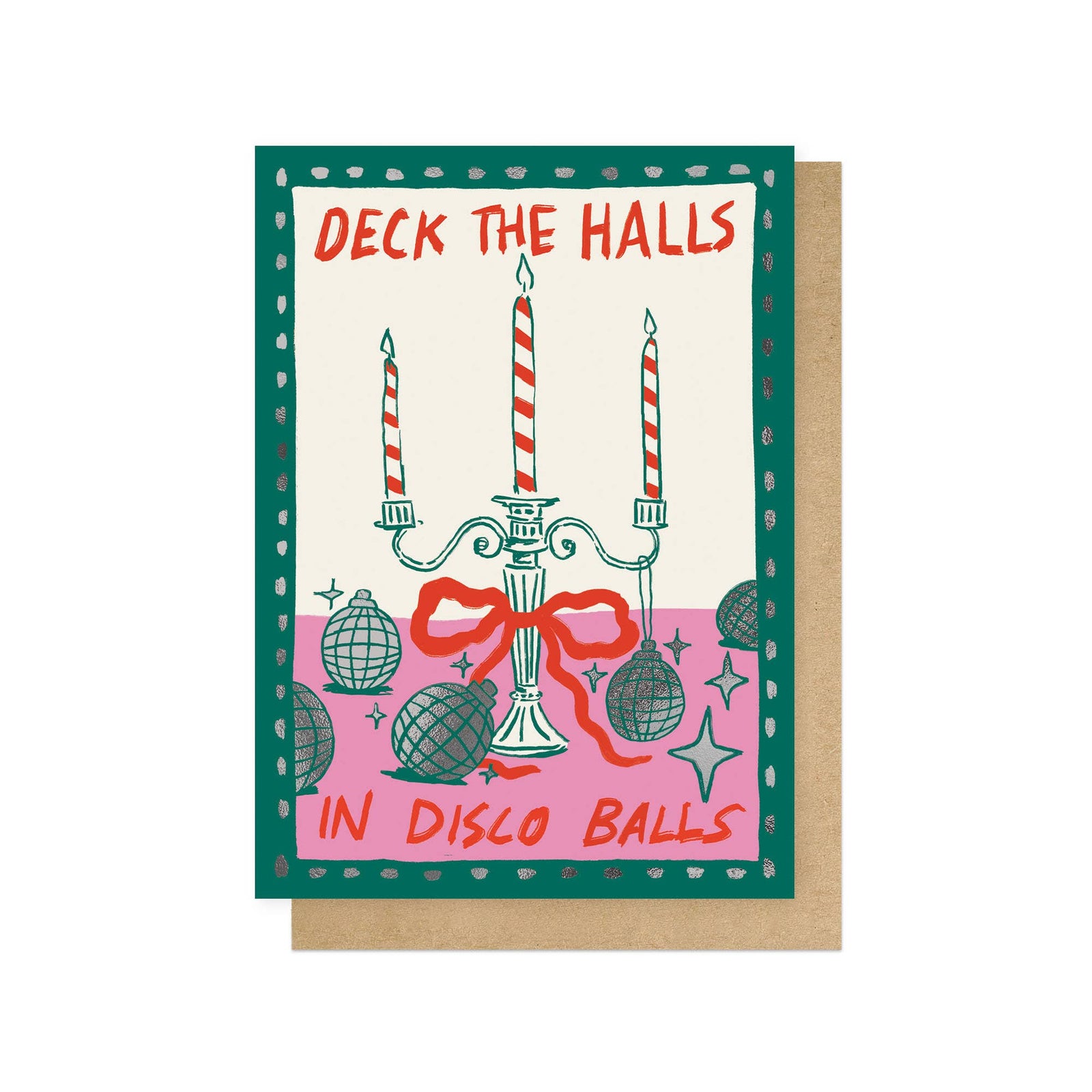 A christmas greeting card with a festive illustrated design featuring a candelabra, disco balls, stars, and the text 'DECK THE HALLS IN DISCO BALLS' on a cream background, with a green border. A kraft paper envelope is partially visible behind it on a white background.