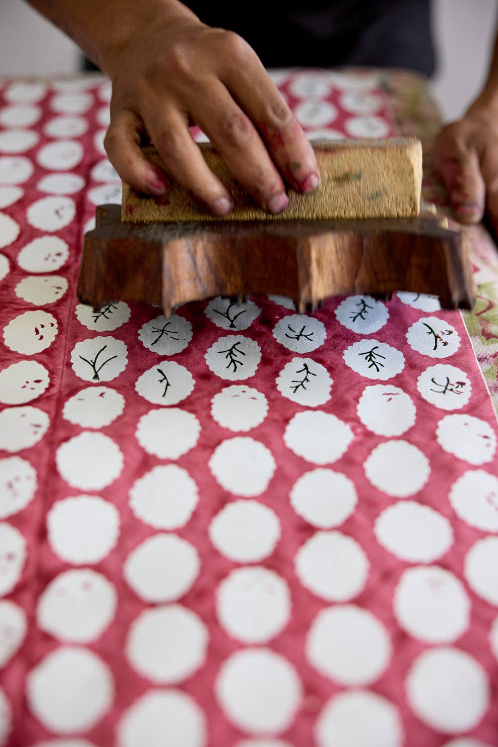 Person using a wooden block to print patterns on wrapping paper with a red and white scalloped Christmas design.