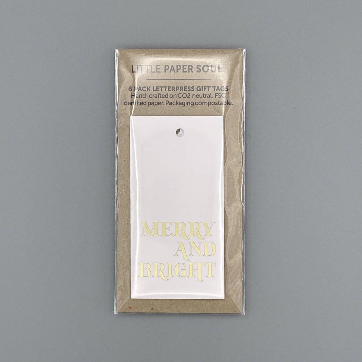 A packaged set of six letterpress gift tags from Little Paper Soul, featuring a white tag with 'MERRY AND BRIGHT' in gold foil on a neutral kraft paper backing, shot against a solid gray background.