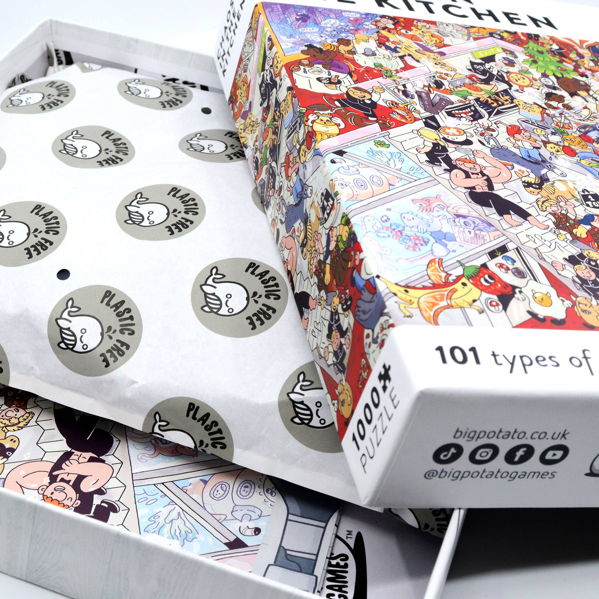 A colourful jigsaw puzzle box labeled '1000+ PUZZLE' and '101 types of' is shown open with printed puzzle pieces and packaging paper inside. The box artwork is highly detailed and cartoon-style, and the inside packaging features repeated round stickers reading 'PLASTIC FREE.