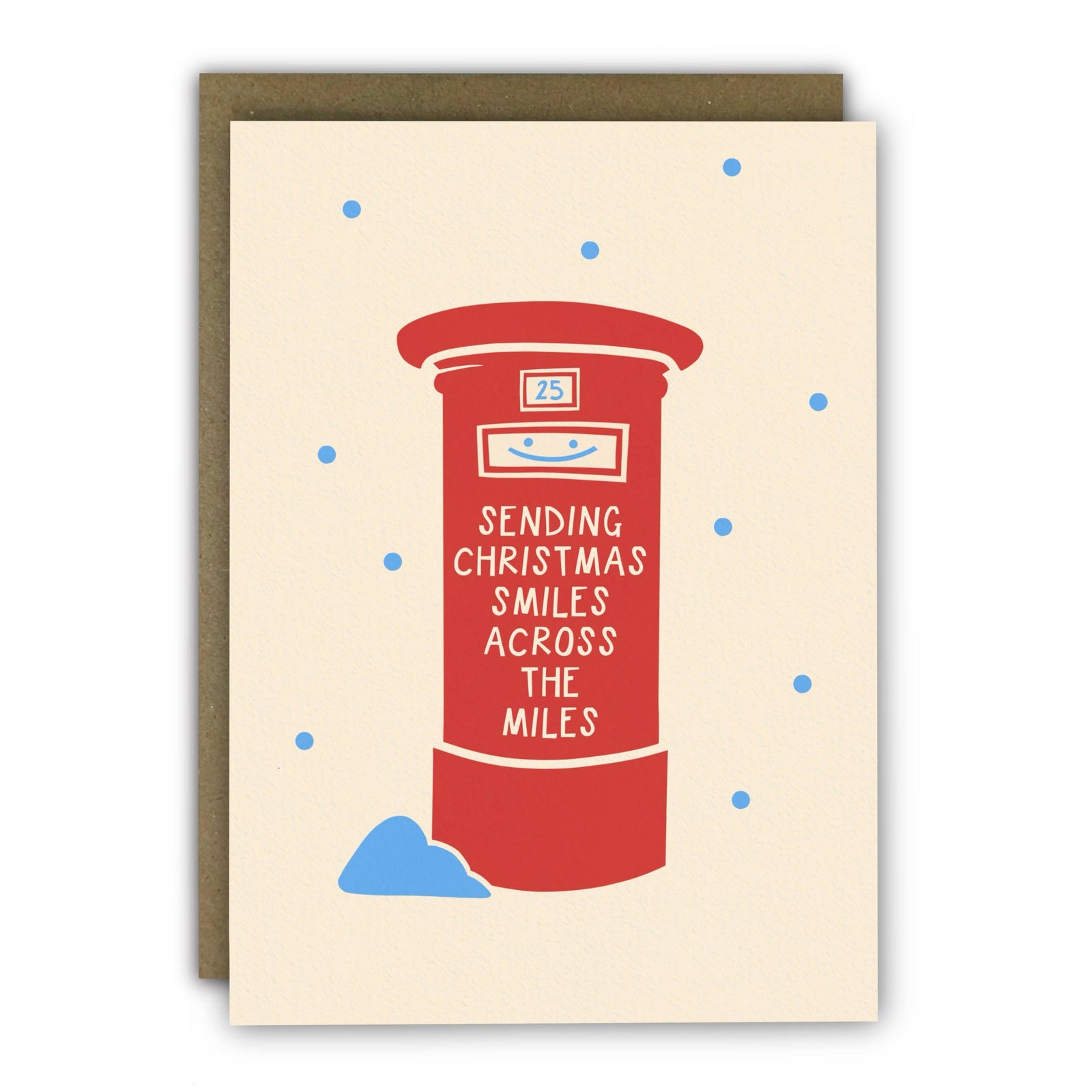 A Christmas greeting card featuring a red post box illustration with the text 'SENDING CHRISTMAS SMILES ACROSS THE MILES' and small blue snow dots on a cream background, shown with a brown envelope behind it.