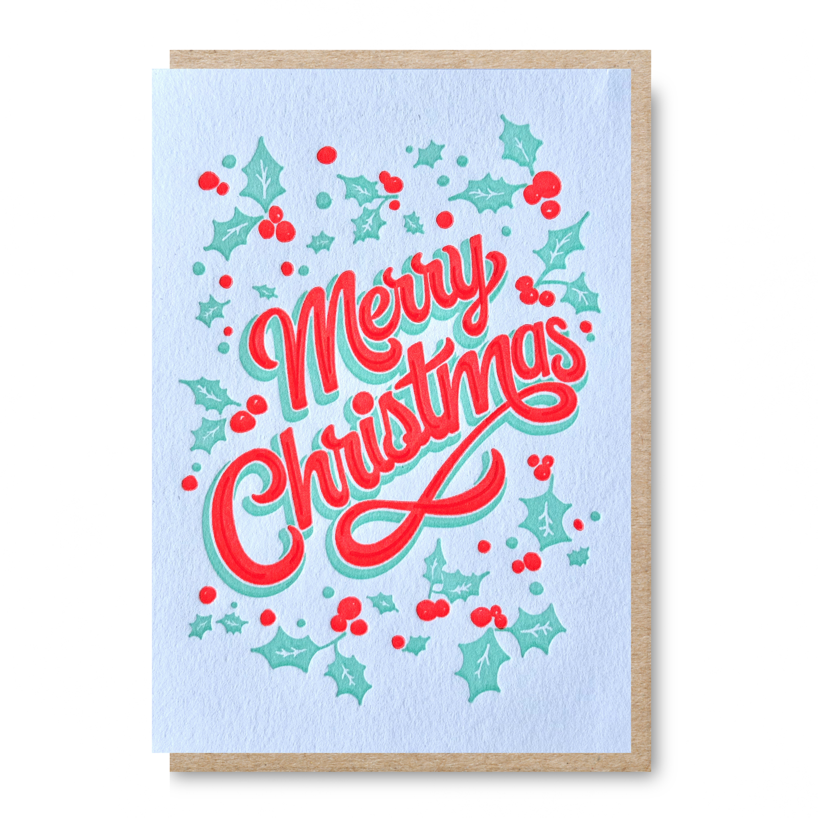 An A6 Christmas greeting card with a kraft paper envelope, featuring the words 'Merry Christmas' in red cursive with a mint green outline, surrounded by red berries and mint green holly leaves on a cream background.