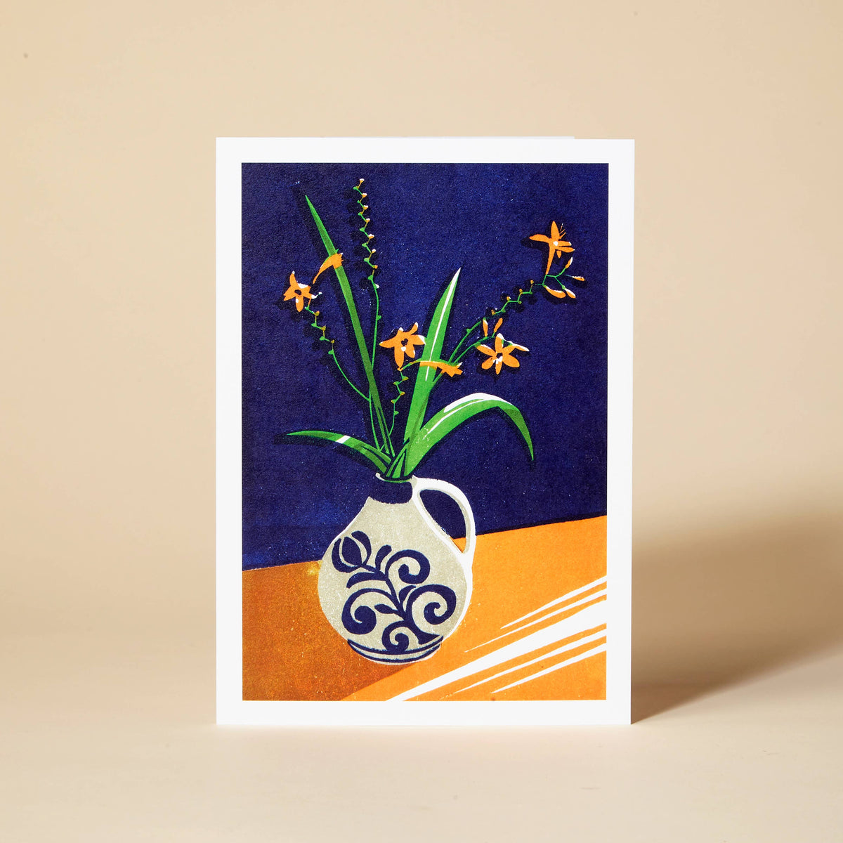 A greetings card with a blue and white vase of crocosmia flowers design on a blue and orange background