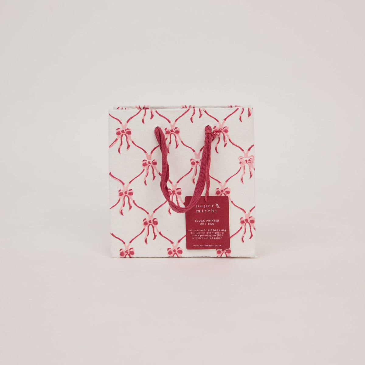 A small Christmas gift bag with a Christmas Bows pattern on a light gray background by paper mirchi at penny black