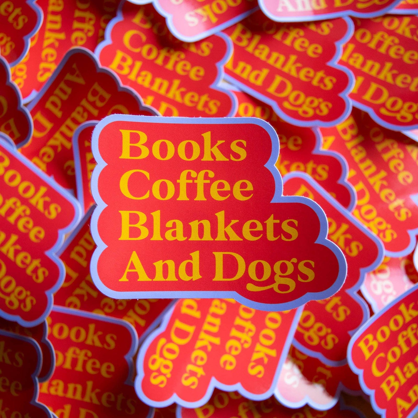 Stack of 'Books Coffee Blankets And Dogs' stickers with red and yellow text.
