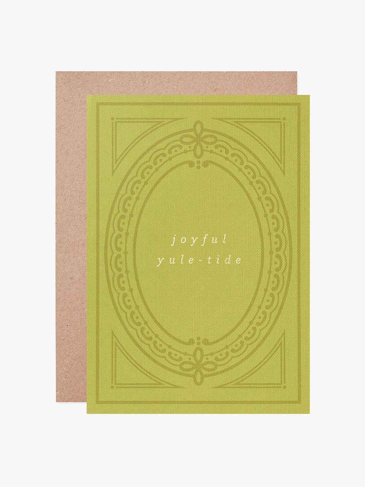 An A6 greeting card with a muted yellow-green front featuring an ornate oval border and the words 'joyful yule-tide' in the centre, shown with a plain kraft paper envelope behind it on a light gray background.