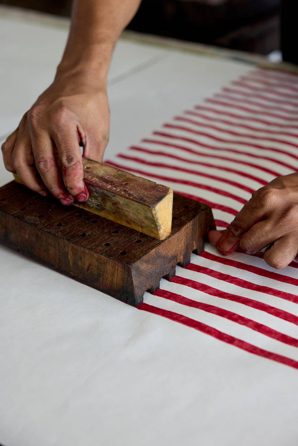 Person using a wooden block to print red lines on a white wrapping paper with red stripes.