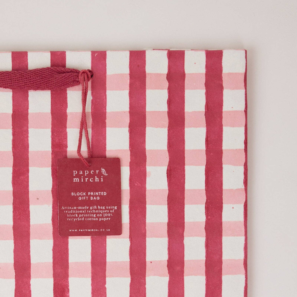 A close up of a large christmas gift bag with pink plaid design on a light gray background by paper mirchi at penny black