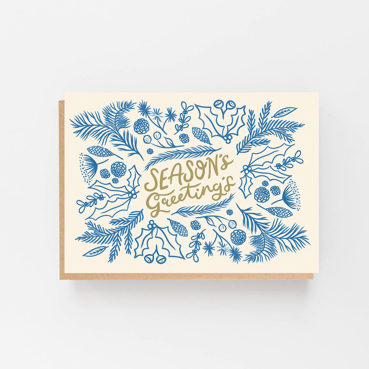 A cream-coloured greetings card with a kraft paper envelope behind, featuring blue botanical illustrations and the words 'SEASON'S GREETINGS' in gold script, shown on a light grey background.