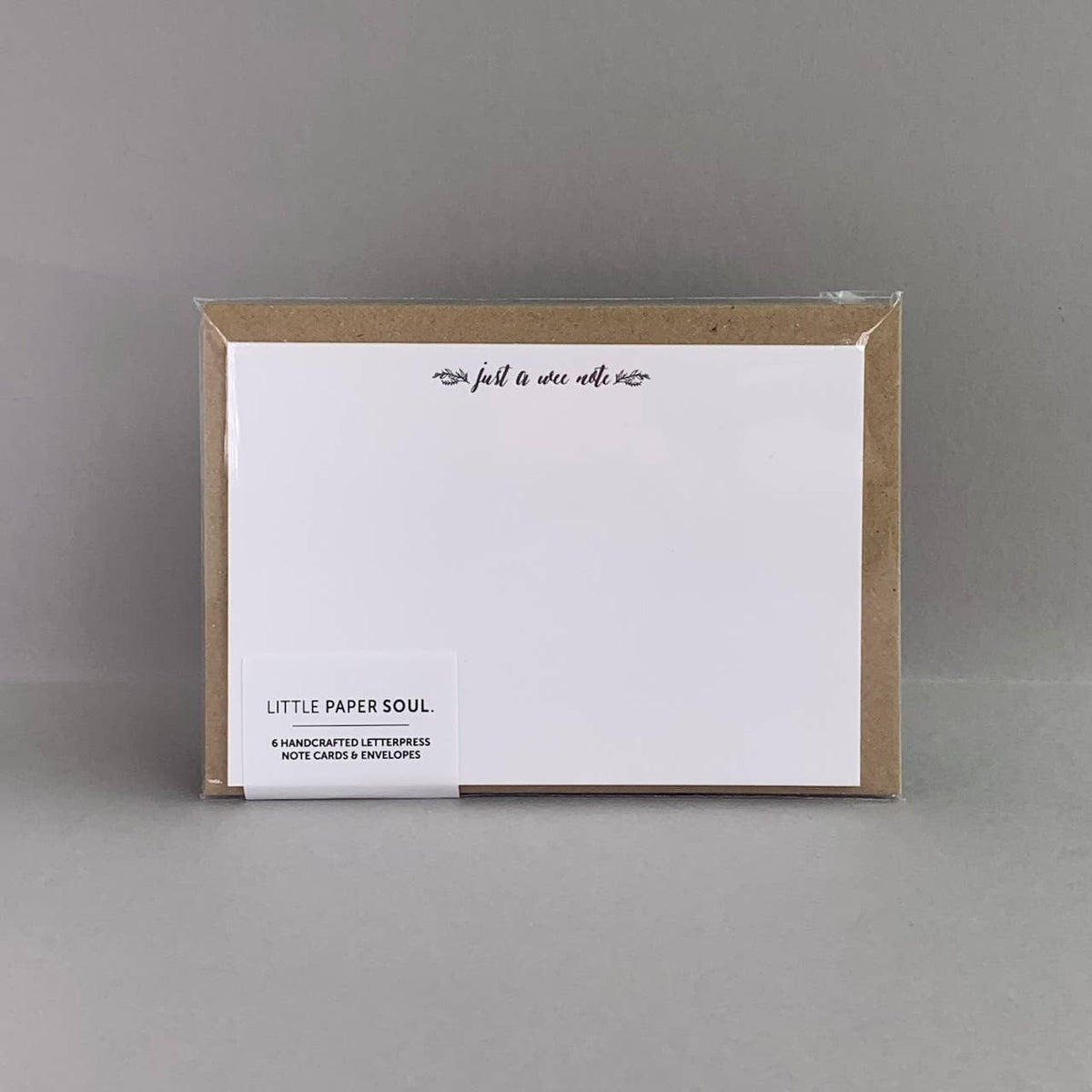 A pack of white letterpress notecards with a kraft envelopes, packaged in a clear plastic sleeve and displayed on a neutral gray background. The brand 'Little Paper Soul' is visible on the lower left label.