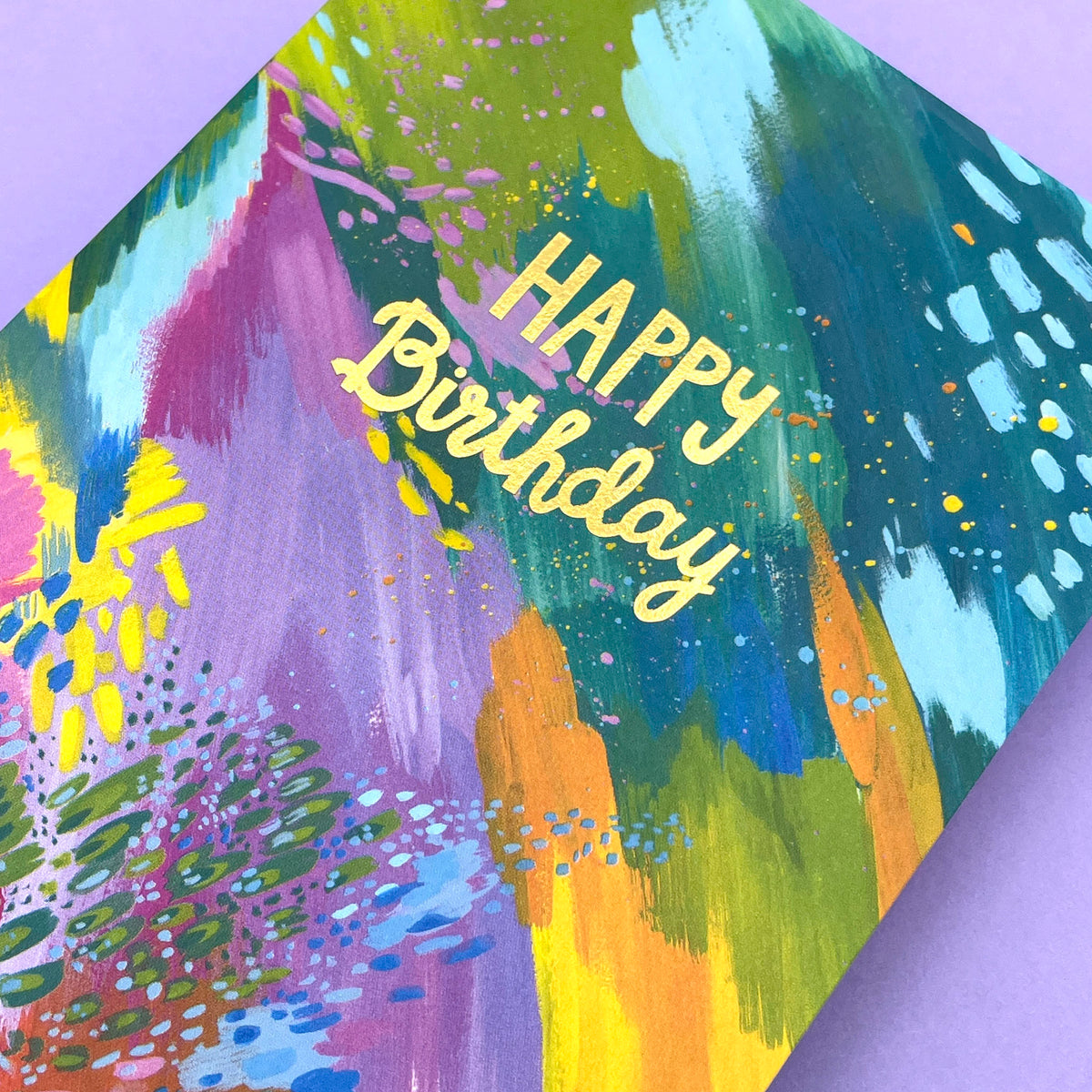 A colourful abstract painted greetings card to celebrate a birthday. The writing in the centre of the card is gold foil cursive writing stating &#39;Happy Birthday&#39;.