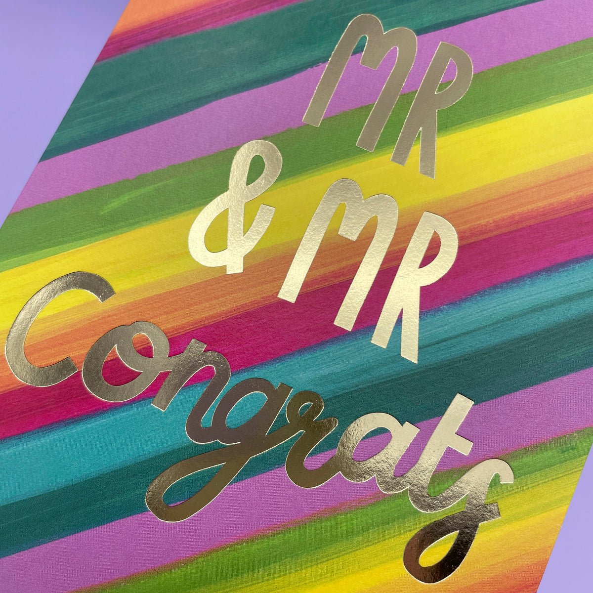 A colourful rainbow stripe greetings card to celebrate a wedding. The rainbow stripes are diagonal across the card and the writing in the centre of the card is big gold foil stating &#39;Mr &amp; Mr Congrats&#39;.