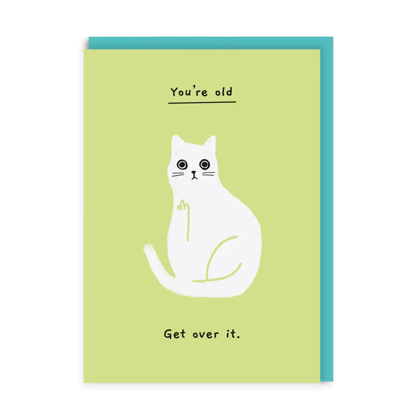 A lime green greetings card with an illustration of a white cat on it. Above the cat is the underlined handwriting in black saying &#39;You&#39;re old&#39; and below the cat it says &#39;Get over it.&#39; A teal envelope is shown to accompany the card.