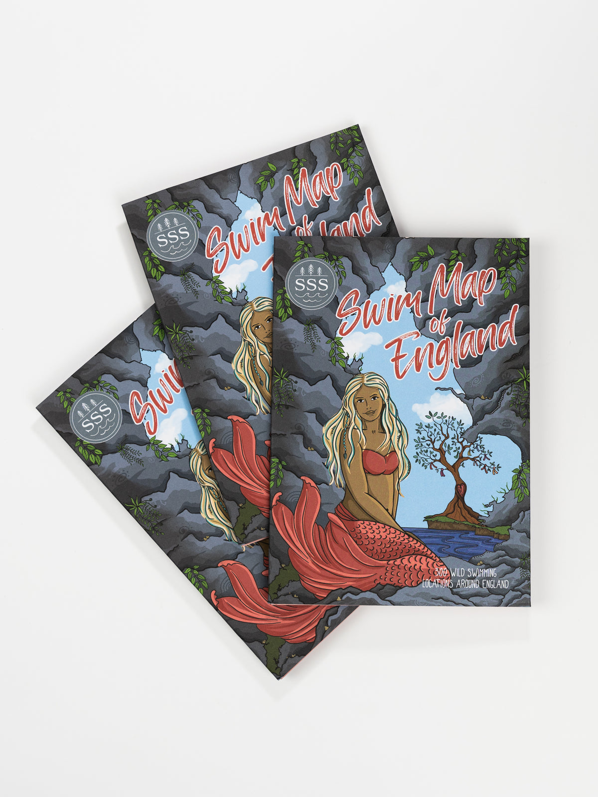 Three front covers of a swim map of England, showing a mermaid at the entrance to a cave. The mermaid has long blonde hair, brown skin colour and a red tail.