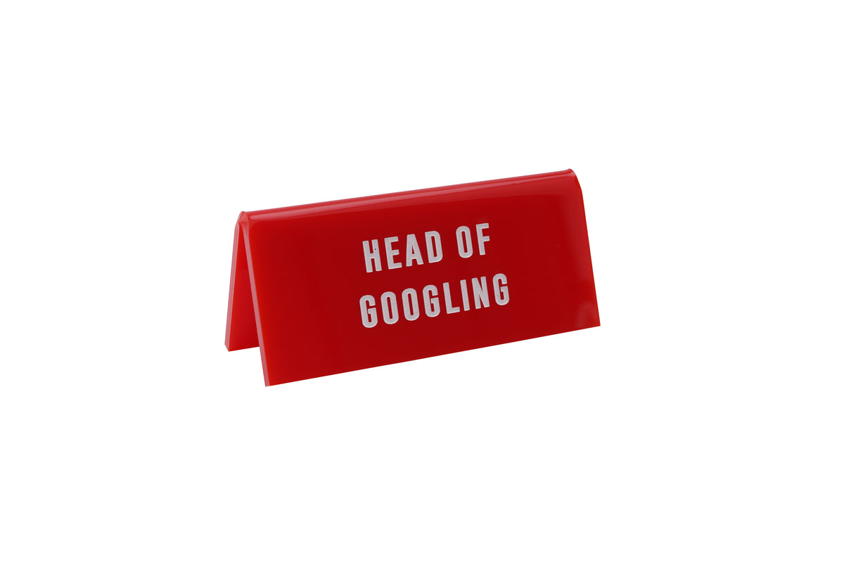 A small RED acrylic sign that has in big white capital letters on it &#39;HEAD OF GOOGLING&#39;.