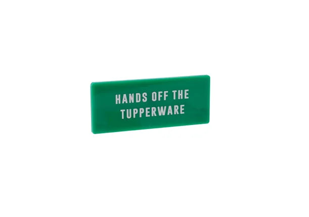 A rectangular green fridge magnet with the words HANDS OFF THE TUPPERWARE in white capitals.