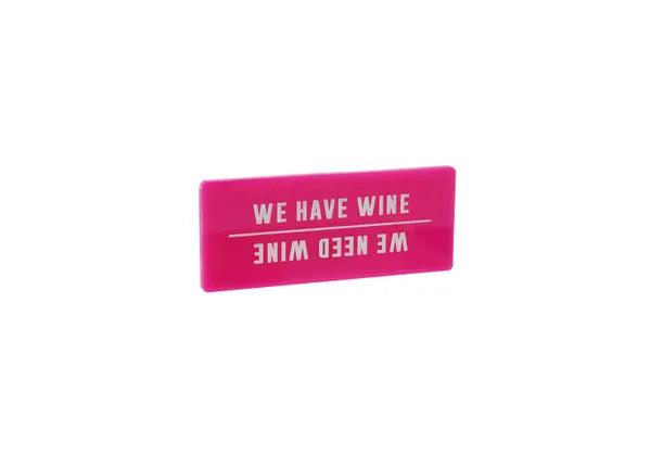A rectangular pink fridge magnet with the words WE HAVE WINE in white capitals. And if you turn it upside down it reads WE NEED WINE, separated by a thin white line.