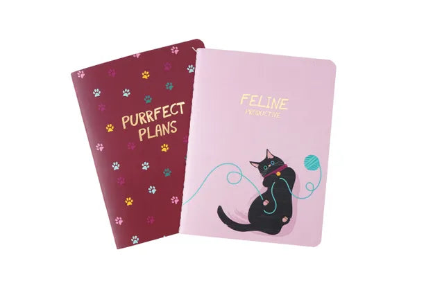 An image of two thread bound notebooks with a cat theme. One is burgundy with the words in gold &#39;purrfect plans&#39; and the other is baby pink wiht a black cat playing with a ball of wool with gold writing saying &#39;feline productive&#39;.
