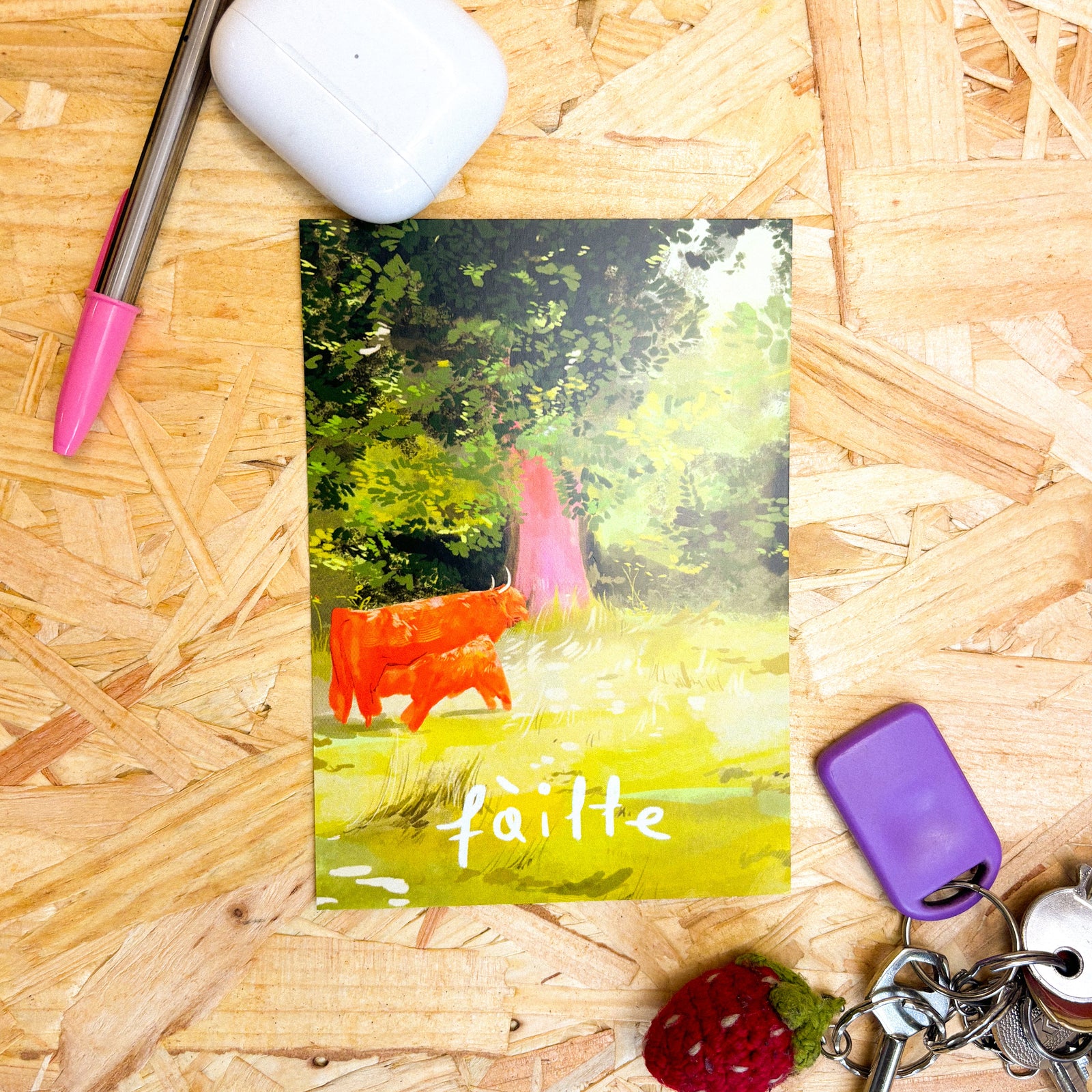 Failte Highland Cow Illustrated Postcard shown on a table with keys