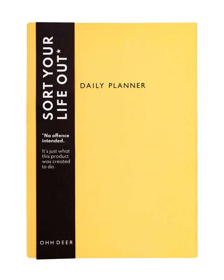 The front cover of a daily planner by Ohh Deer. The cover design is a bright and warm light pastel yellow colour. There are black embellished words saying in capitals 'DAILY PLANNER'. The image shows a black belly band including details about the product.