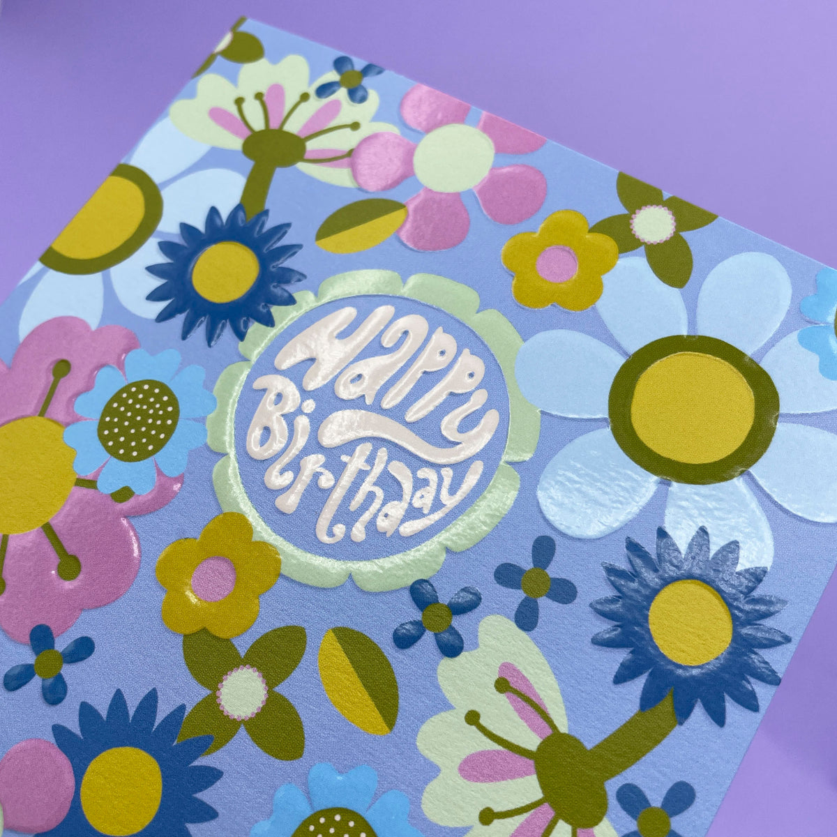 A colourful floral greetings card to celebrate a birthday where the main colour is blue. The wording in the centre of the card is &#39;Happy Birthday&#39;.