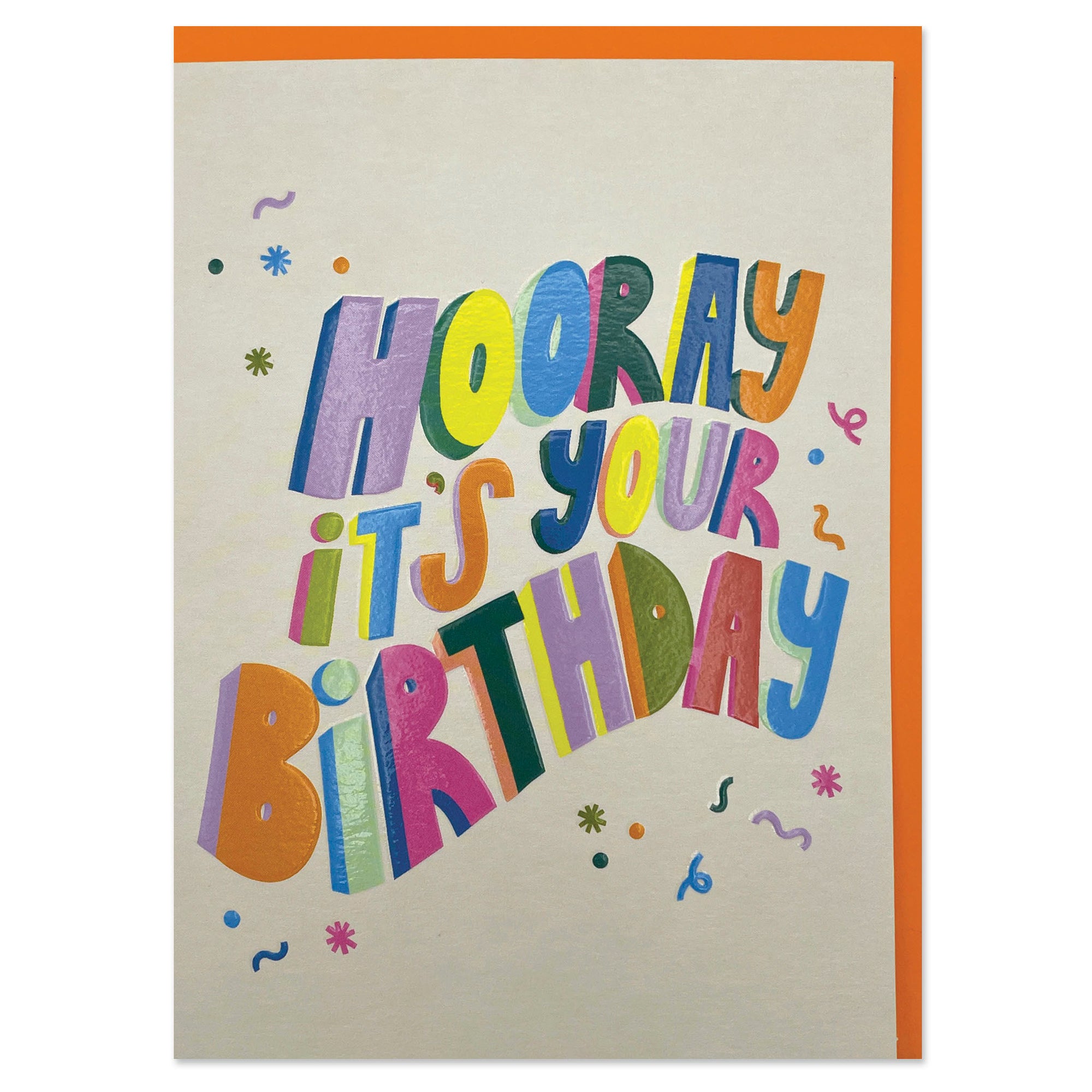 A cream coloured greetings card for a birthday, with a bright orange envelope. It has big wavy colourful words across the front saying in 3D capital letters 'hooray it's your birthday'. There is some confetti flying around the words too.