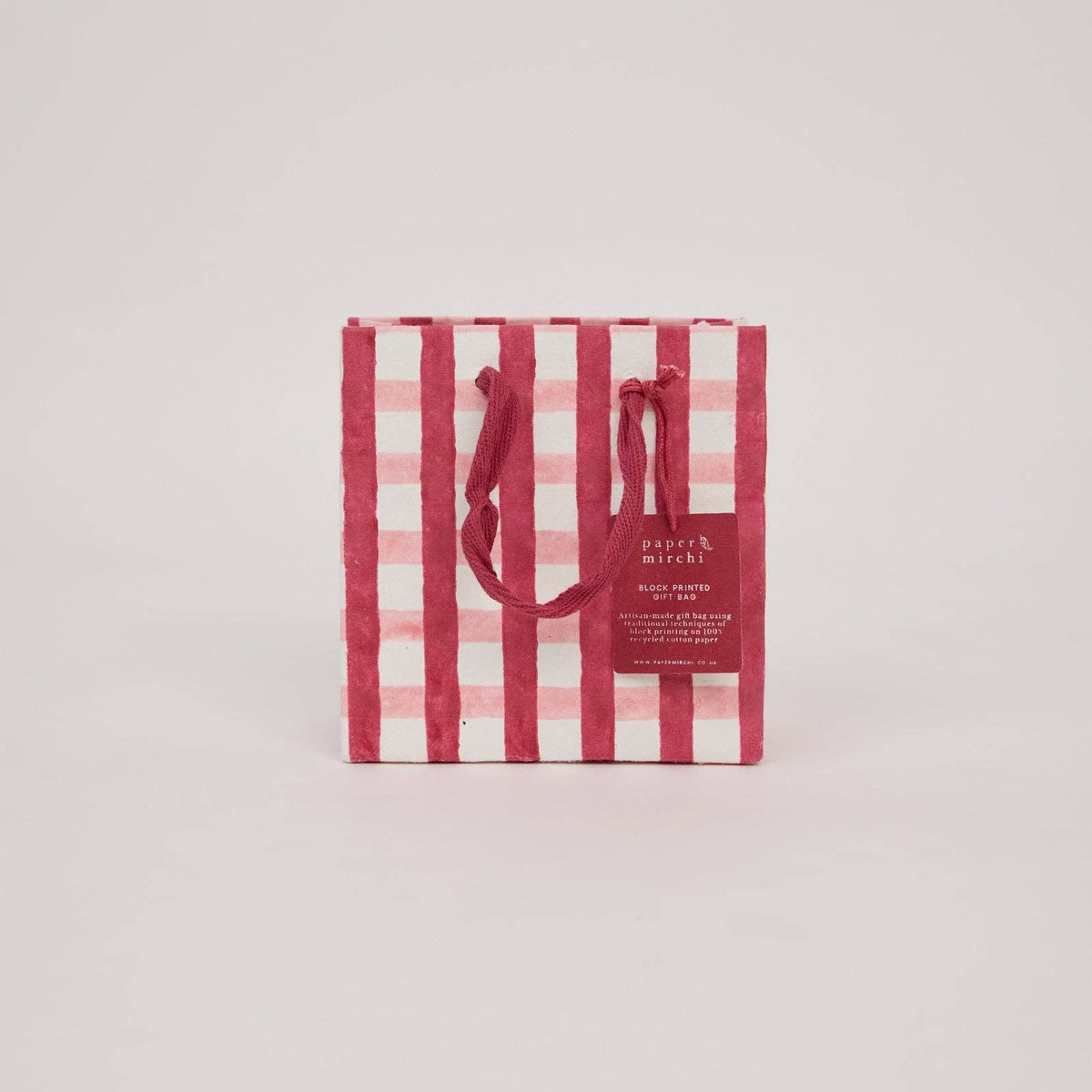 A small Christmas gift bag with a pink and red plaid pattern on a light gray background by paper mirchi at penny black