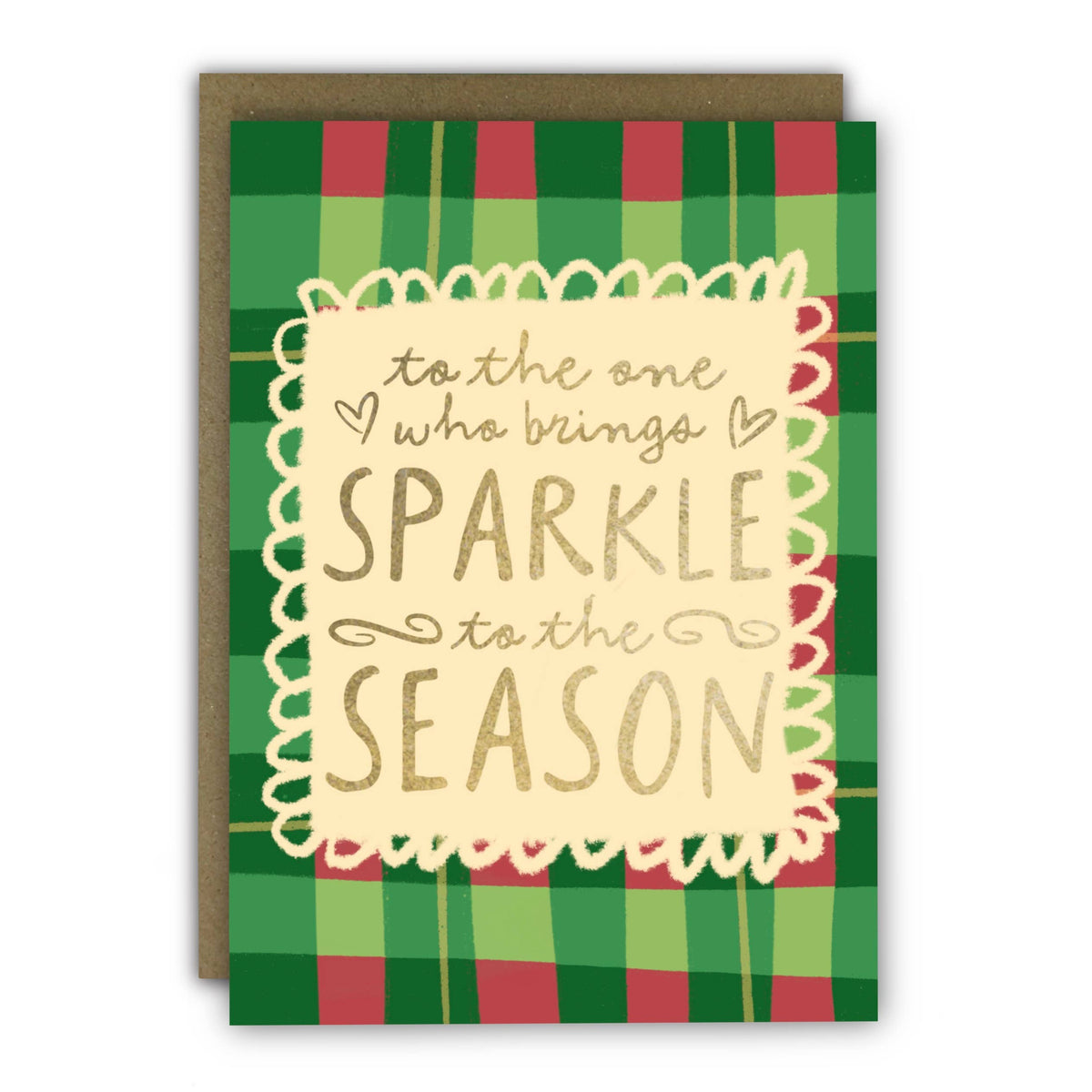 A holiday greeting card with a green and red plaid pattern, featuring a cream scalloped border and gold foil text that reads 'to the one who brings SPARKLE to the SEASON'. A brown kraft envelope is behind the card at penny black