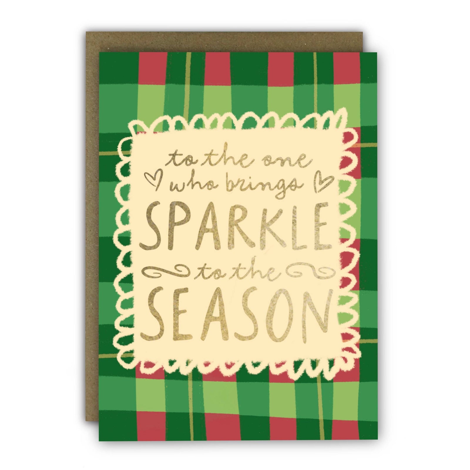 A holiday greeting card with a green and red plaid pattern, featuring a cream scalloped border and gold foil text that reads 'to the one who brings SPARKLE to the SEASON'. A brown kraft envelope is behind the card at penny black