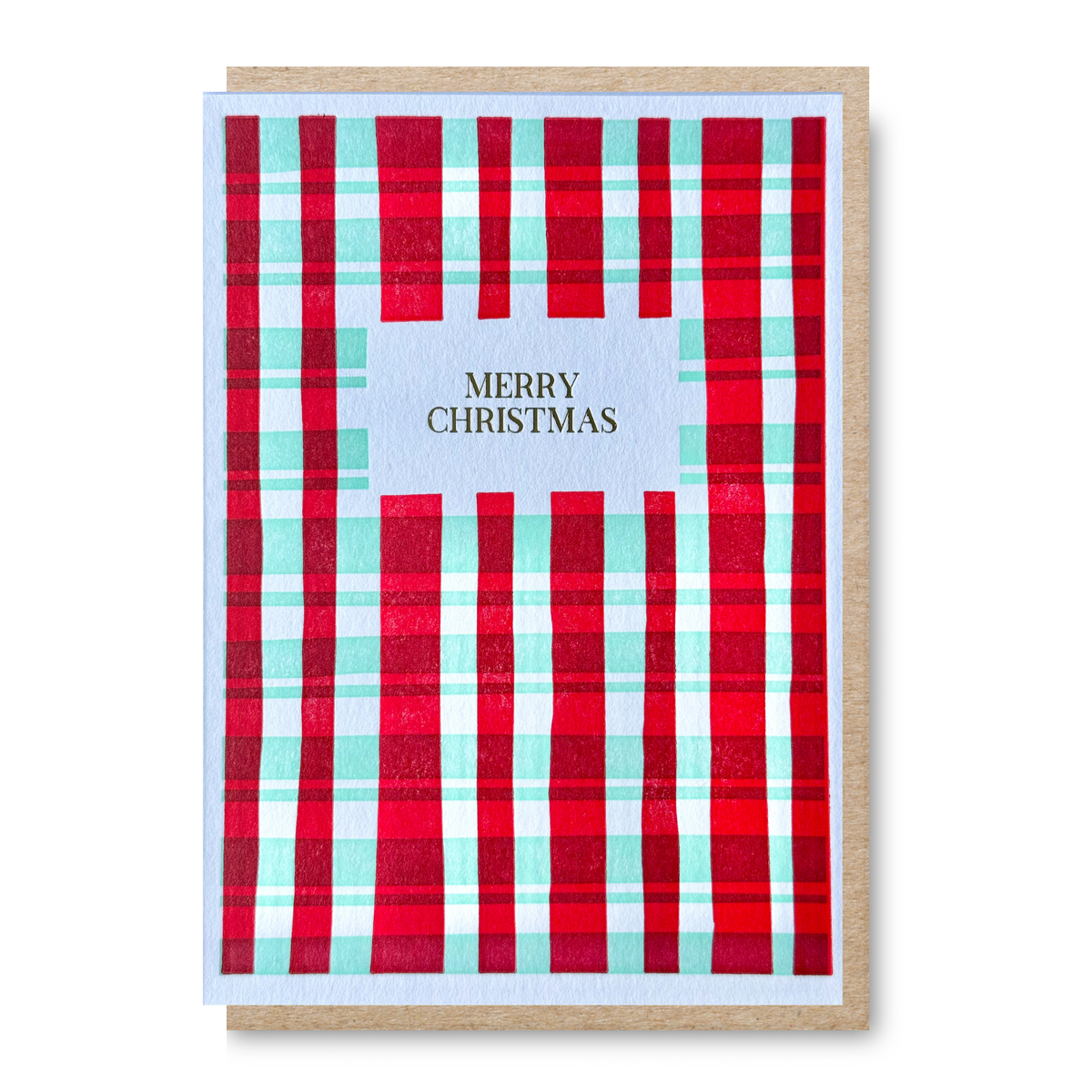 A Christmas greeting card with a red, mint green, and white plaid pattern border, featuring a centre panel with the text 'MERRY CHRISTMAS' in gold. The card is shown with a kraft paper envelope behind it on a white background.